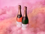 Bottles of Noughty alcohol-free sparkling rosé and Noughty non-alcoholic sparkling Chardonnay stood together in a pink and yellow cloud
