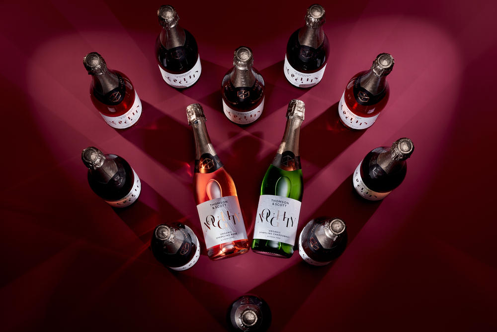 noughty alcohol free chardonnay and rose bottles arranged in a heart shape against a red background